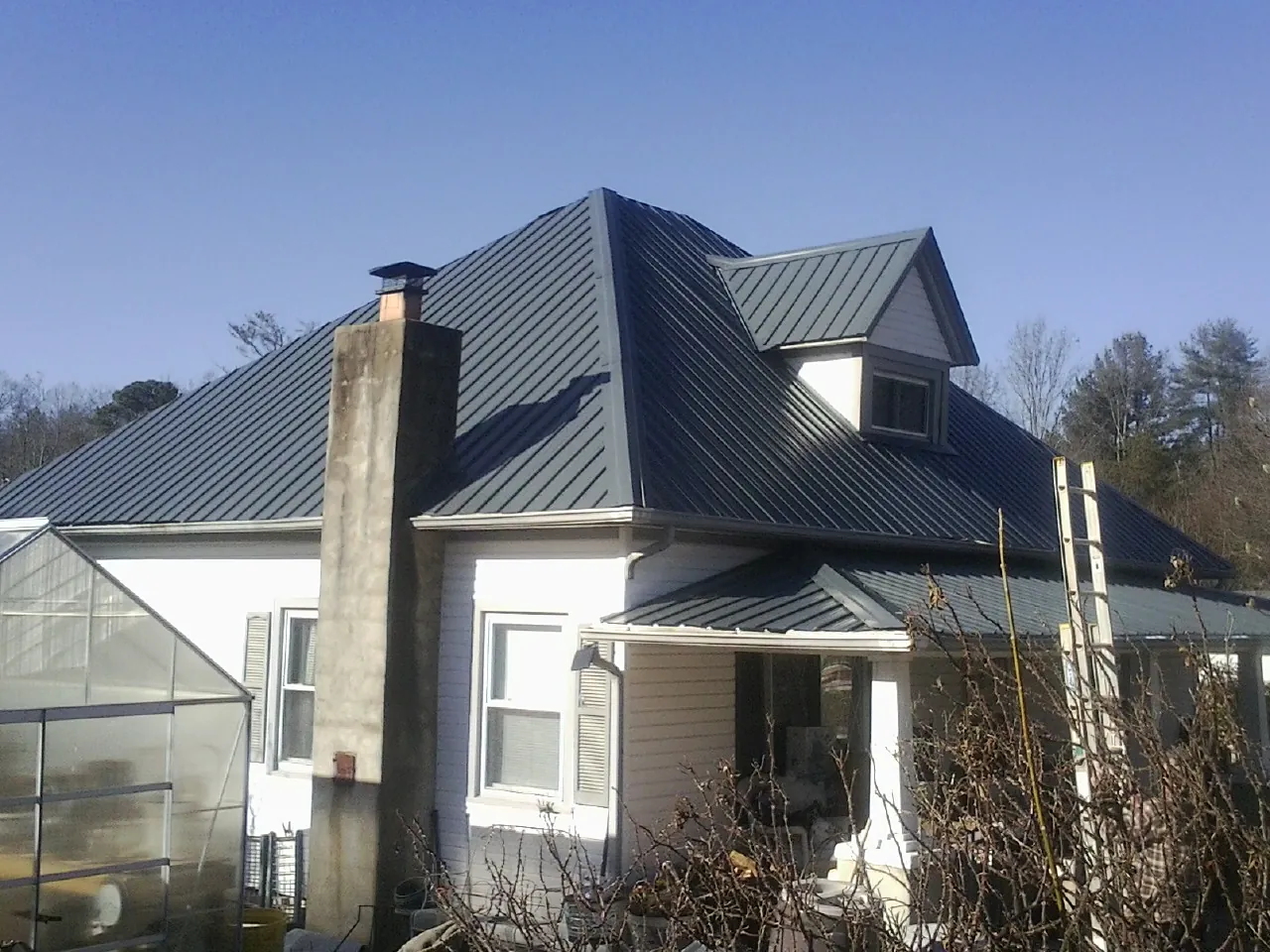 Dark blue standing seam metal roof on a white farmhouse with dormer — Slate & Tile Roof Repair by Roofing Brothers in Wataga