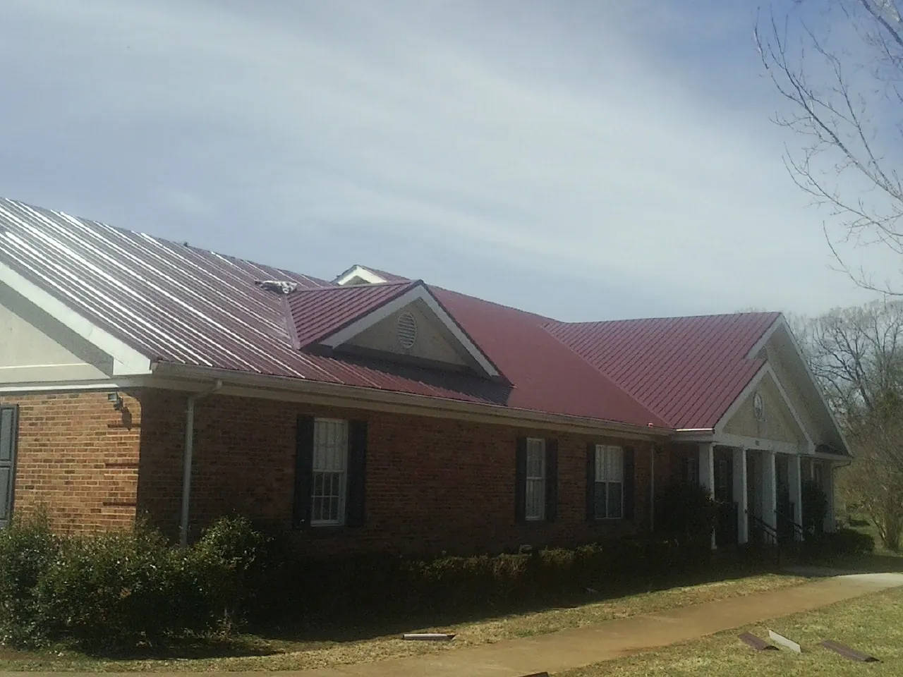 Red metal roof with gabled entries on a long brick building, from a Hail Damage Roof Repair job in Wataga