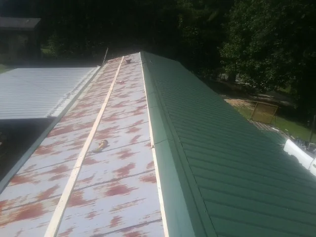 Old rusted panels beside newly installed green metal roofing — Wind Damage Roof Repair by Roofing Brothers in Wataga