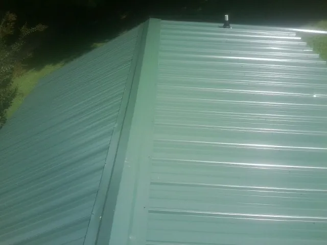 New green metal panels meeting at the ridge of a roof — Flat Roof Repair work by our crew in Wataga