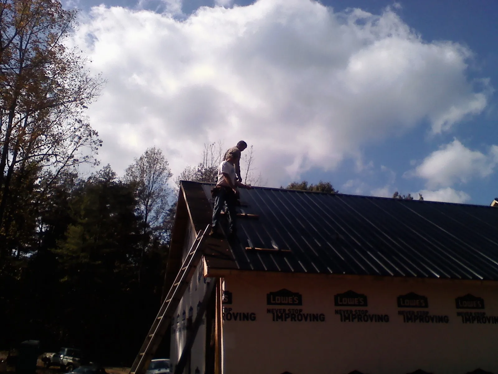 Roofer fastening dark metal panels high against a cloudy sky, from a Roof Inspection job in Wataga