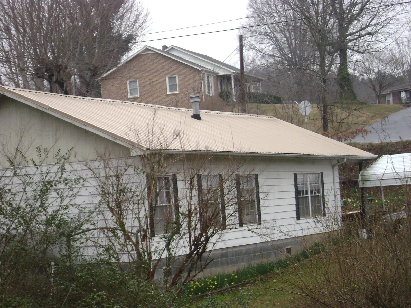 Tan metal roof on a white sided house set into a hillside — Commercial Roofing by Roofing Brothers in Wataga