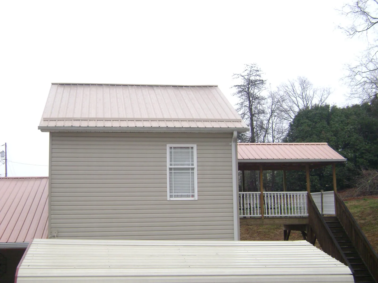 Tan metal roofs on a two story addition and attached porch, from a Roof Replacement job in Wataga